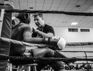 Wide shot of a strength coach talking to a boxer in a boxing ring motivating him.