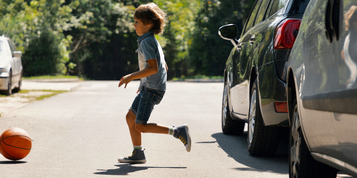 boy running into street chasing basketball.